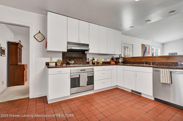 kitchen with dark tile patterned floors, dark countertops, appliances with stainless steel finishes, white cabinets, and under cabinet range hood