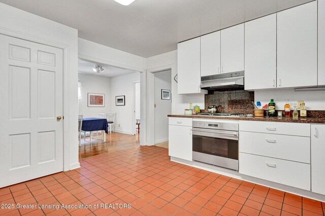 kitchen with decorative backsplash, light tile patterned flooring, under cabinet range hood, white cabinets, and appliances with stainless steel finishes