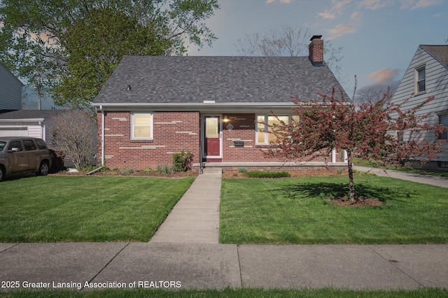 view of front facade with a shingled roof, a chimney, a front yard, and brick siding