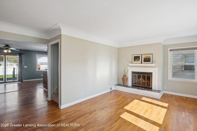 unfurnished living room with visible vents, wood finished floors, a fireplace, baseboards, and ceiling fan