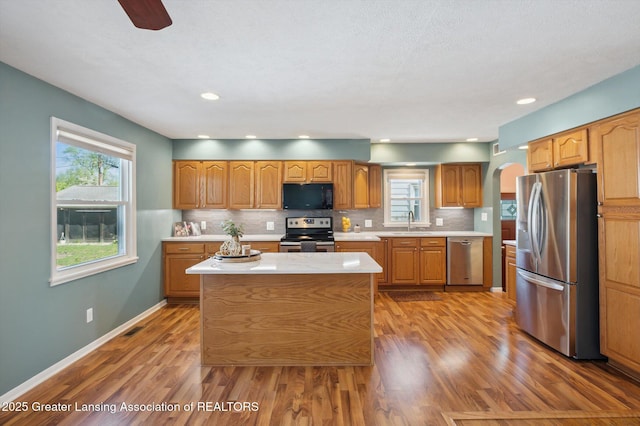 kitchen featuring wood finished floors, light countertops, arched walkways, a sink, and appliances with stainless steel finishes