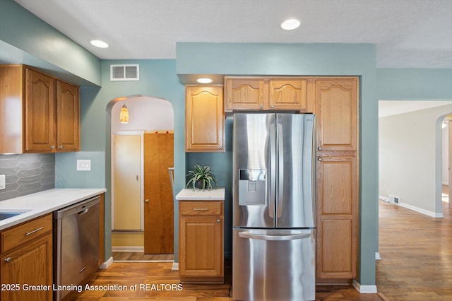 kitchen featuring arched walkways, stainless steel appliances, wood finished floors, tasteful backsplash, and visible vents