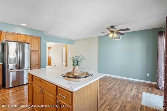 kitchen featuring ceiling fan, light stone countertops, stainless steel fridge, wood finished floors, and visible vents