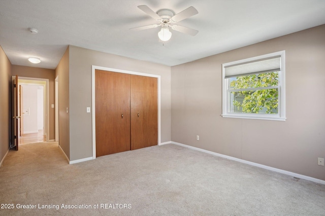 unfurnished bedroom with baseboards, light colored carpet, ceiling fan, and a closet