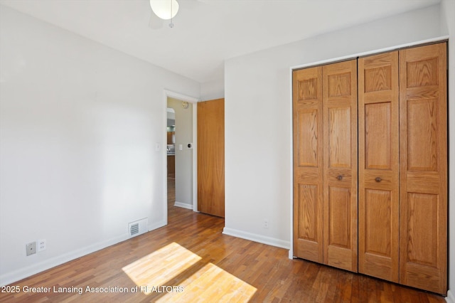 unfurnished bedroom with baseboards, visible vents, wood finished floors, and a closet