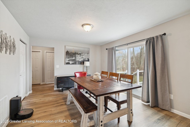 dining area featuring baseboards, light wood-type flooring, a textured ceiling, and visible vents