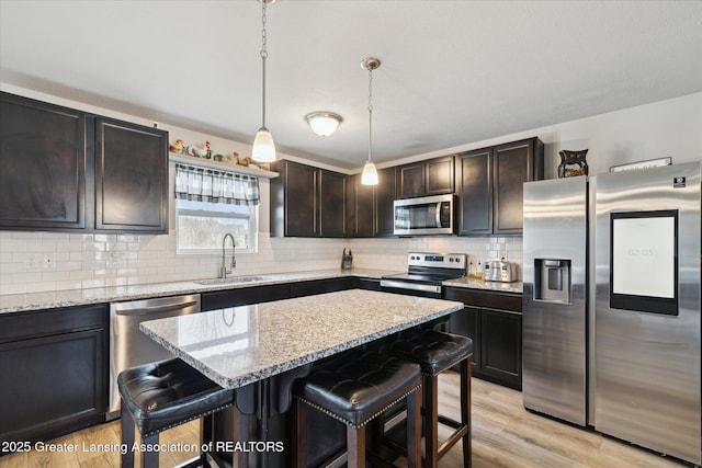 kitchen with a kitchen breakfast bar, decorative backsplash, appliances with stainless steel finishes, light wood-type flooring, and a sink