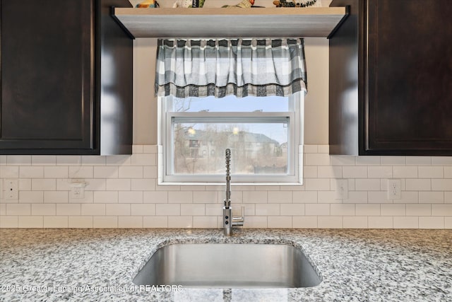 details with dark brown cabinets, light stone countertops, a sink, and tasteful backsplash