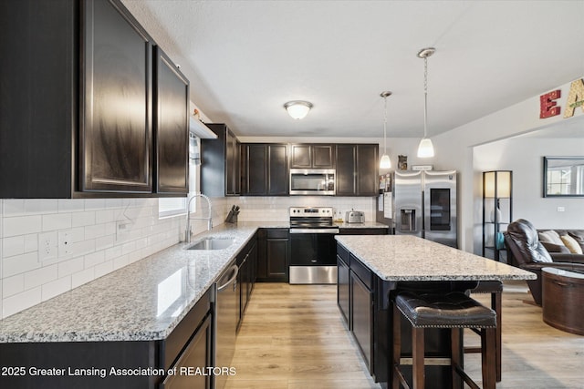 kitchen featuring a sink, stainless steel appliances, open floor plan, a kitchen bar, and backsplash