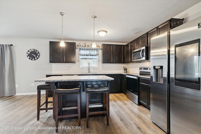 kitchen with appliances with stainless steel finishes, tasteful backsplash, light wood finished floors, and a kitchen breakfast bar