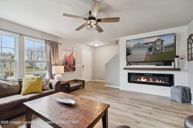 living area with a glass covered fireplace, wood finished floors, baseboards, ceiling fan, and a textured ceiling