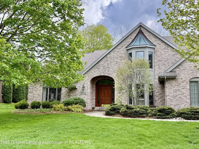 tudor-style house featuring a shingled roof, a front yard, and brick siding