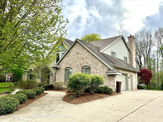 view of front facade featuring a garage, a chimney, brick siding, a shingled roof, and driveway