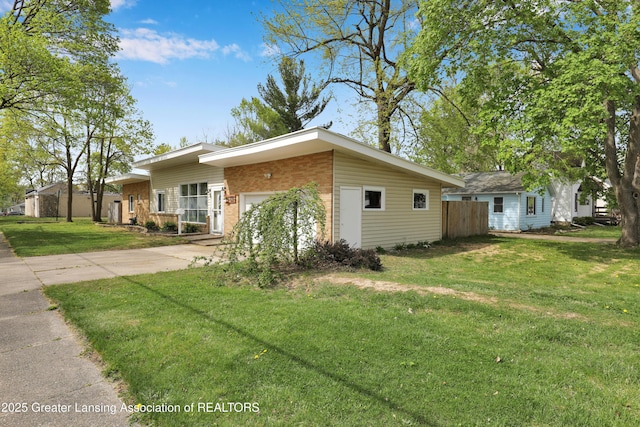 view of side of property featuring fence, brick siding, a garage, a lawn, and driveway