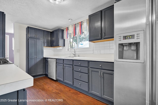 kitchen featuring dark wood-style flooring, a textured ceiling, tasteful backsplash, a sink, and stainless steel appliances