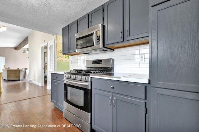 kitchen featuring appliances with stainless steel finishes, gray cabinetry, baseboards, light countertops, and dark wood-type flooring