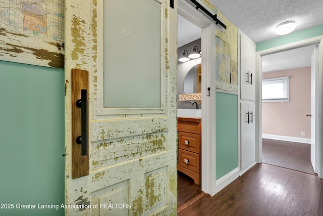 corridor featuring baseboards, a barn door, and dark wood-style flooring