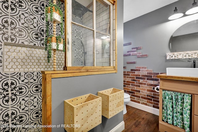 bathroom featuring a tile shower, wood finished floors, vanity, baseboards, and toilet