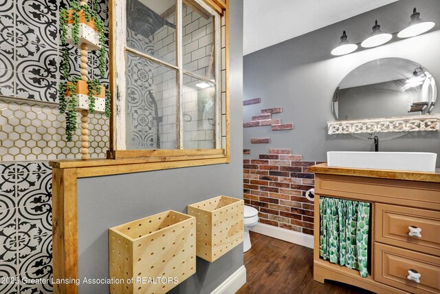 bathroom featuring vanity, wood finished floors, toilet, baseboards, and a tile shower