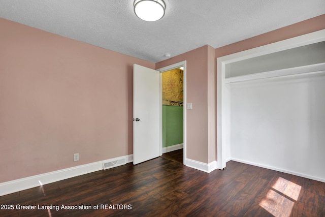 unfurnished bedroom with a textured ceiling, dark wood finished floors, baseboards, visible vents, and a closet