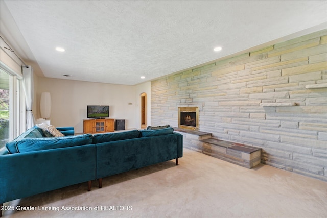 carpeted living room with recessed lighting, a textured ceiling, arched walkways, and a fireplace