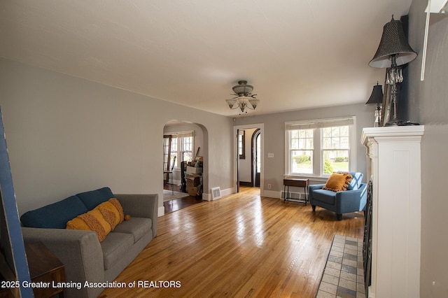 living room with plenty of natural light, arched walkways, light wood-style floors, and visible vents