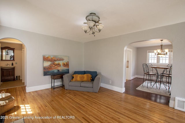 living area with visible vents, arched walkways, wood finished floors, baseboards, and a notable chandelier
