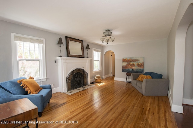 living area featuring arched walkways, baseboards, a healthy amount of sunlight, and light wood finished floors