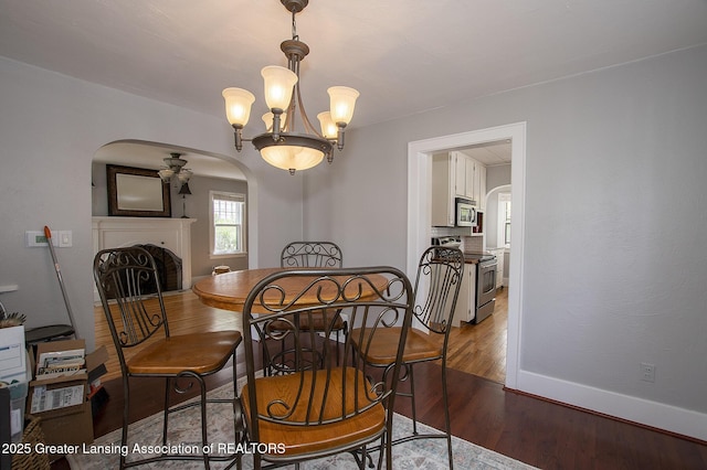 dining space with an inviting chandelier, wood finished floors, a fireplace, baseboards, and arched walkways