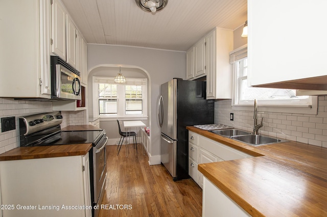 kitchen with tasteful backsplash, a sink, butcher block counters, stainless steel appliances, and white cabinetry