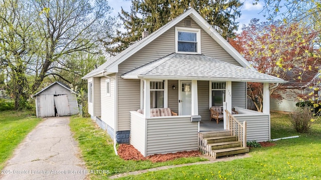 bungalow-style house featuring roof with shingles, a storage shed, a porch, a front yard, and an outbuilding