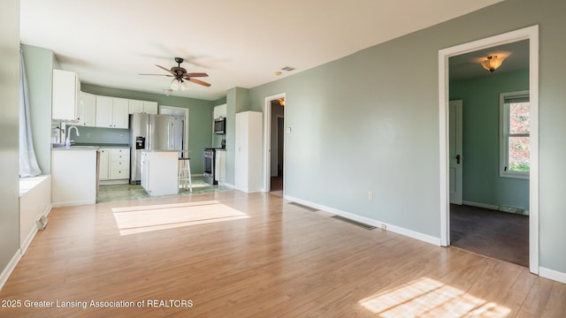unfurnished living room with ceiling fan, a sink, baseboards, light wood-type flooring, and visible vents