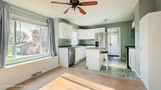 kitchen featuring appliances with stainless steel finishes, a breakfast bar, a sink, light wood-style flooring, and visible vents