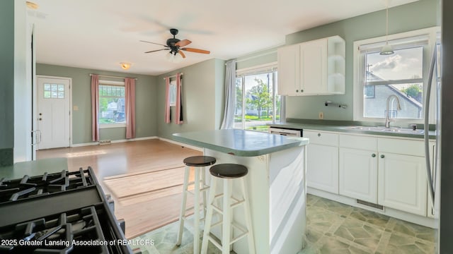 kitchen featuring ceiling fan, a kitchen breakfast bar, white cabinetry, a sink, and decorative light fixtures