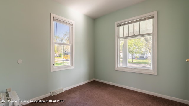 empty room featuring visible vents, baseboards, a healthy amount of sunlight, and dark colored carpet