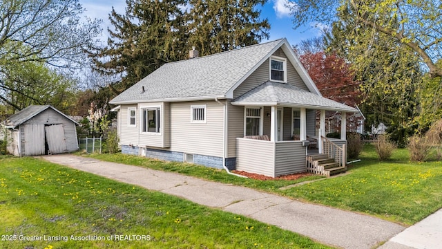 bungalow featuring a porch, a front yard, roof with shingles, an outbuilding, and a storage unit