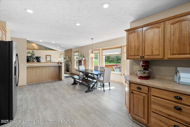 kitchen featuring a textured ceiling, brown cabinetry, freestanding refrigerator, baseboards, and vaulted ceiling