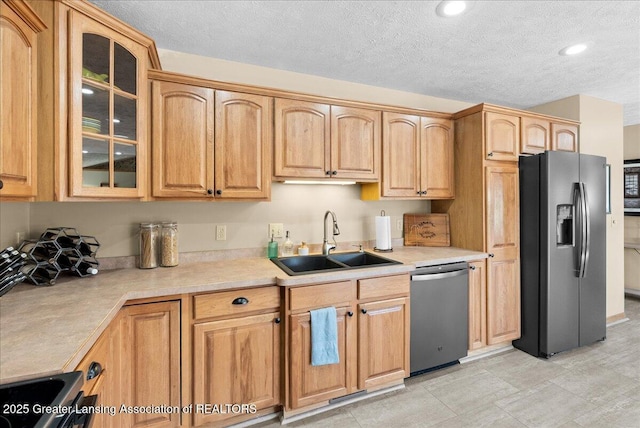 kitchen featuring a textured ceiling, a sink, light countertops, glass insert cabinets, and stainless steel appliances