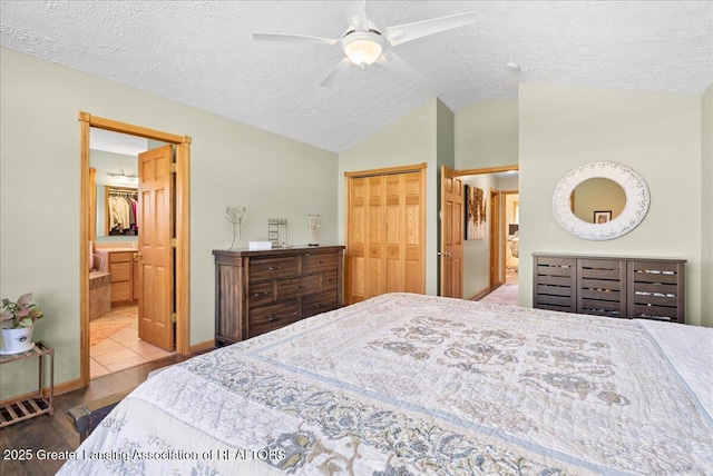 bedroom featuring a closet, a textured ceiling, a ceiling fan, ensuite bath, and vaulted ceiling