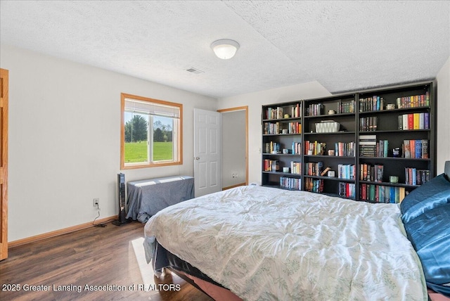 bedroom featuring a textured ceiling, baseboards, visible vents, and wood finished floors