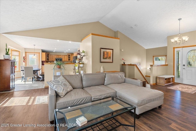 living area with a notable chandelier, vaulted ceiling, a healthy amount of sunlight, and wood finished floors