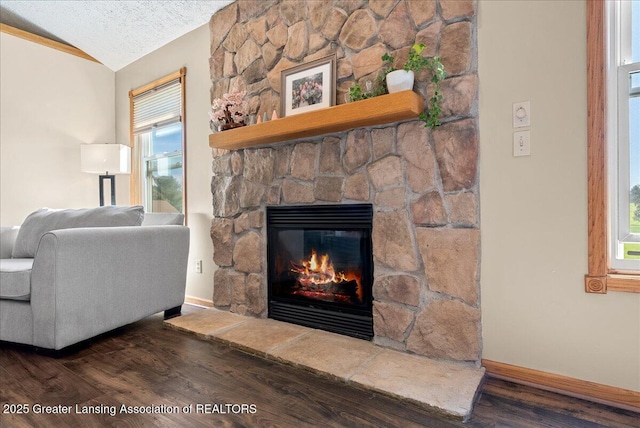 interior space with a textured ceiling, a fireplace, wood finished floors, baseboards, and lofted ceiling