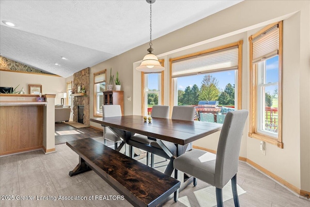 dining room featuring baseboards, a textured ceiling, lofted ceiling, and a fireplace