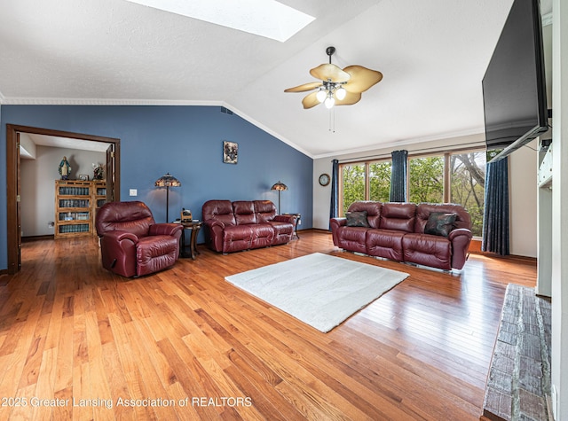 living area with hardwood / wood-style flooring, ceiling fan, and vaulted ceiling with skylight