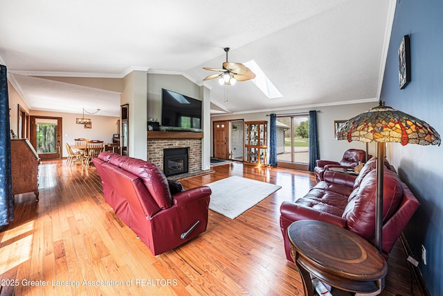 living room featuring a ceiling fan, a healthy amount of sunlight, vaulted ceiling with skylight, and light wood-style floors