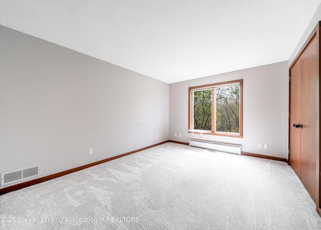 unfurnished bedroom with carpet flooring, a baseboard heating unit, baseboards, and visible vents