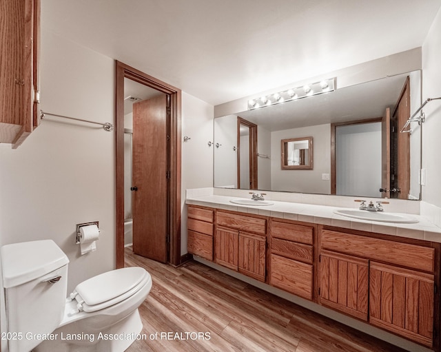 bathroom featuring a sink, double vanity, toilet, and wood finished floors