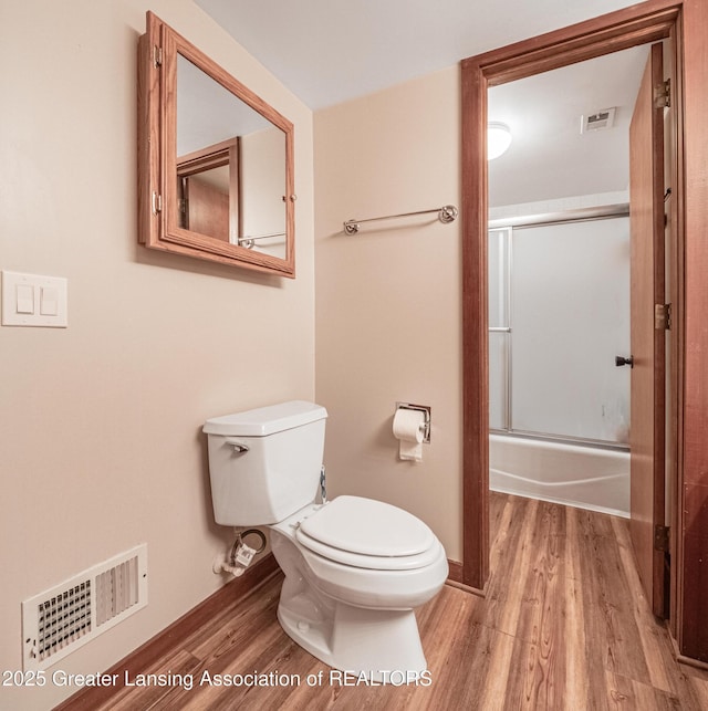 bathroom featuring visible vents, combined bath / shower with glass door, wood finished floors, and toilet