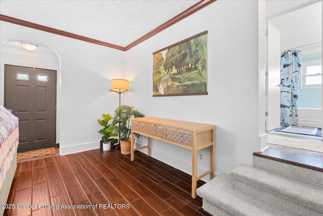 foyer featuring crown molding, baseboards, arched walkways, and wood finished floors