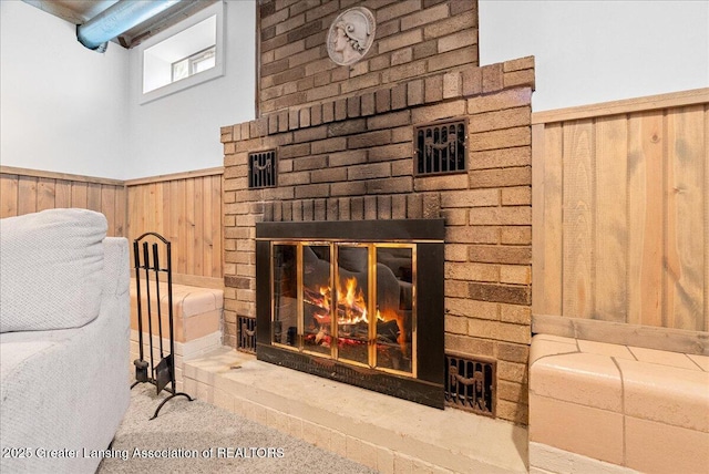 room details with carpet floors, wood walls, wainscoting, and a brick fireplace